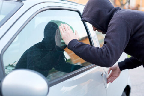 a hooded man breaking into a car