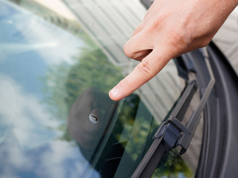 man pointing to hole in car window