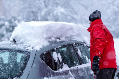 lots of snow on top of car and man standing cleaning it